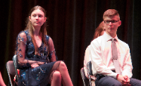two students sit on stage at induction ceremony