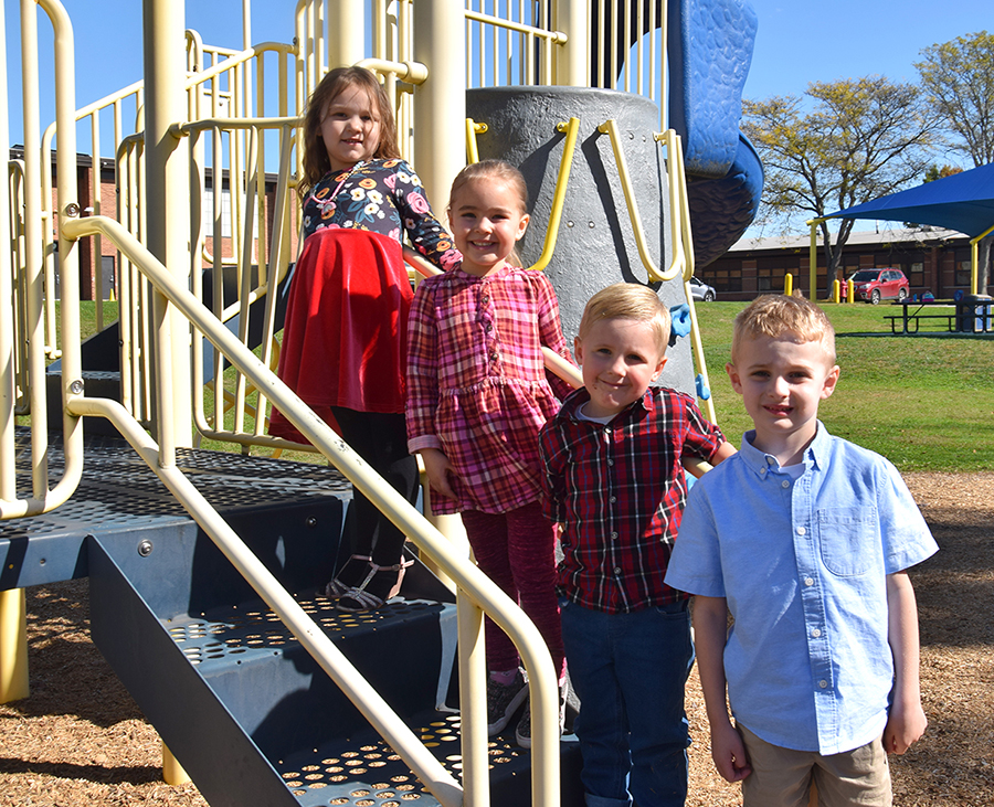 Four Donnelly Elementary students line up on the stairs of a piece of playground equipment.
