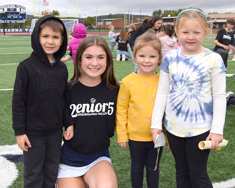 A Susquehanna Valley High School senior with two elementary students on the stadium field.