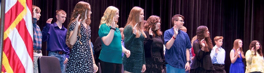 Students being inducted into honor society say pledge with right hands raised