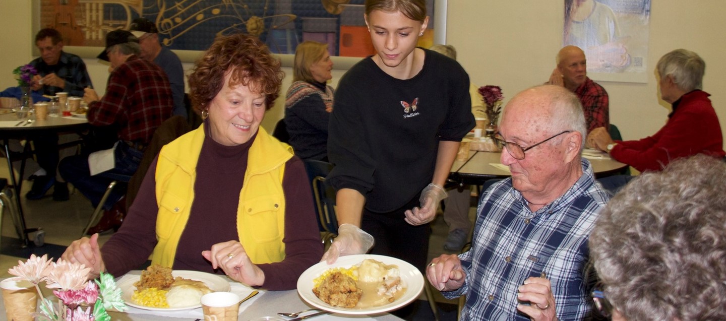 student serves thanksgiving dinner to seniors