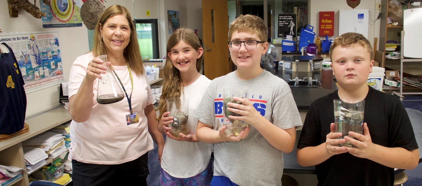 Students show science project with teacher