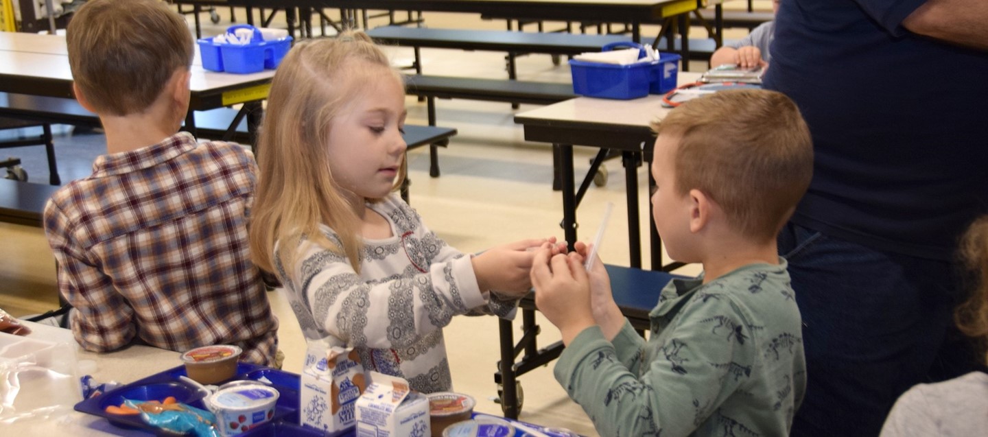 A Brookside Elementary student helps her friend open his snack during lunch in the cafeteria.