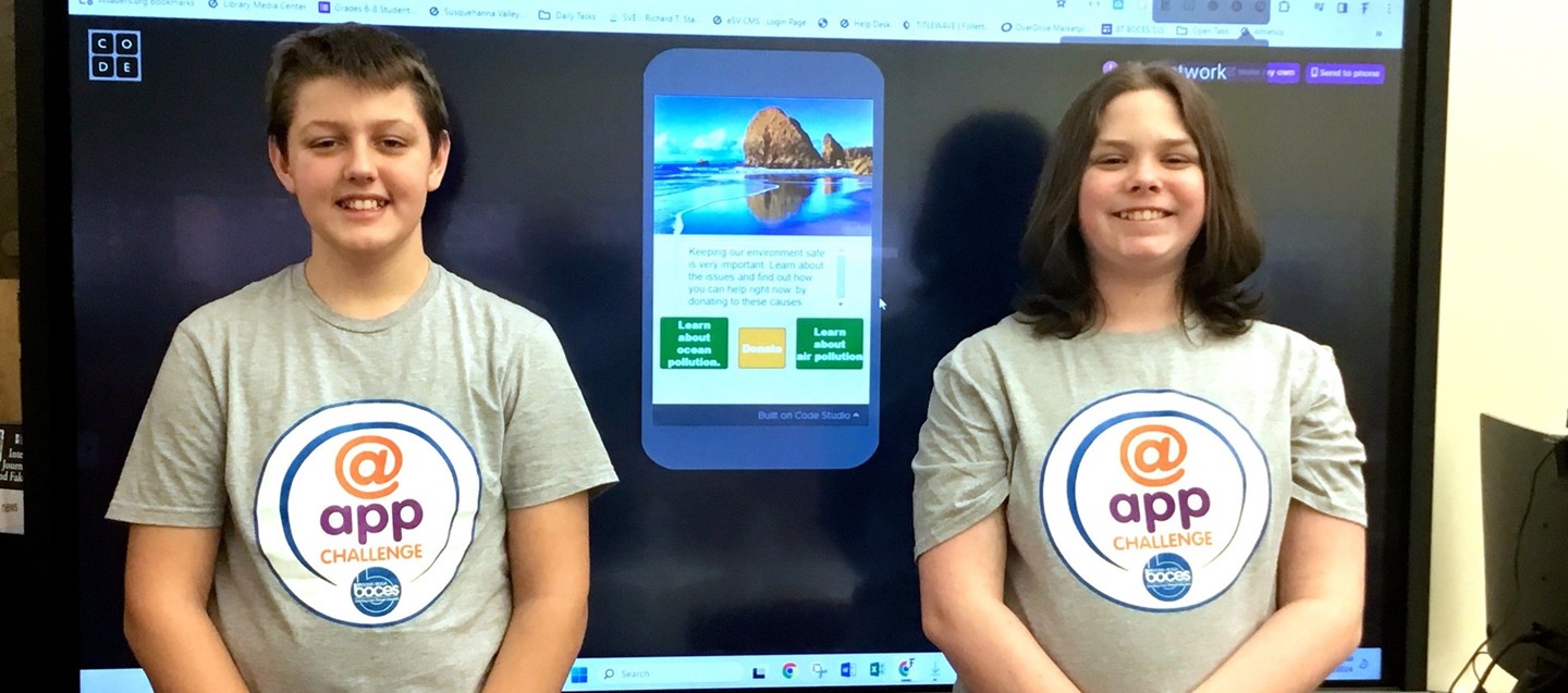 two boys in front of big screen monitor with app challenge t shirts on