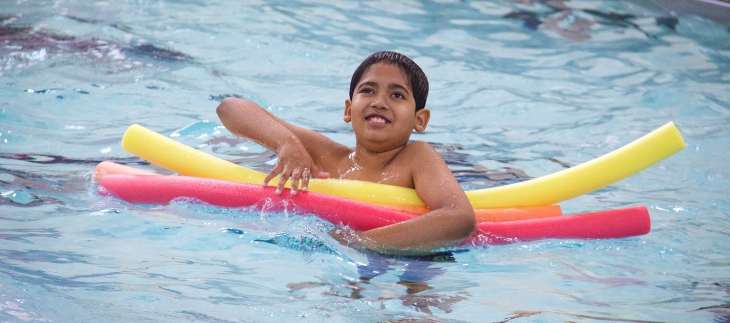 boy in pool with flotation noodles