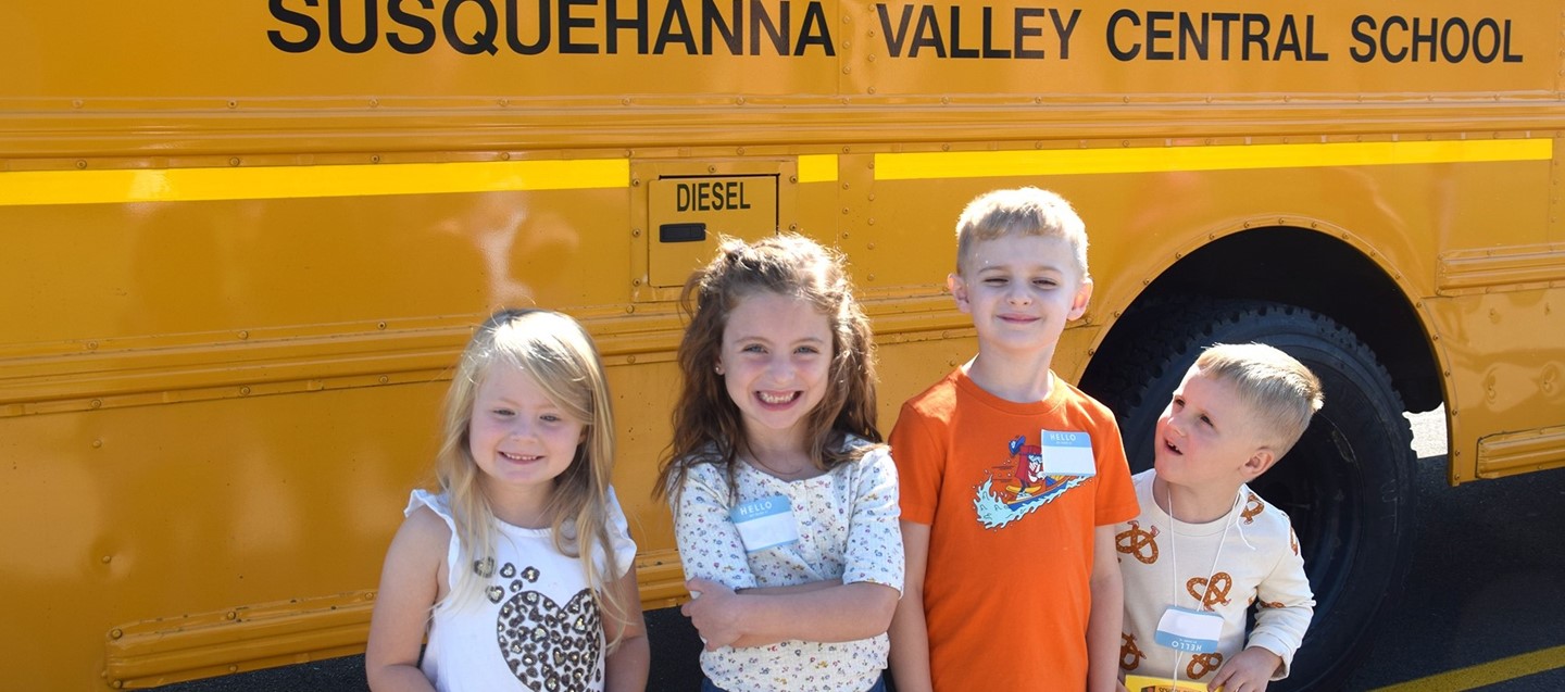 Four Kindergarten students lined up by a school bus after having a ride during orientation.