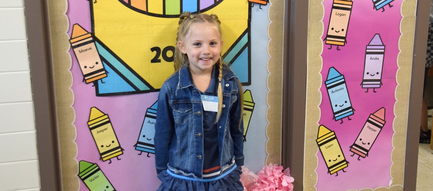 A Kindergarten student stands in front of a backdrop of giant crayons during orientation at Donnelly Elementary.