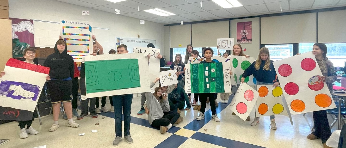 Sixth graders in Saber Success class hold up board game designs they created.