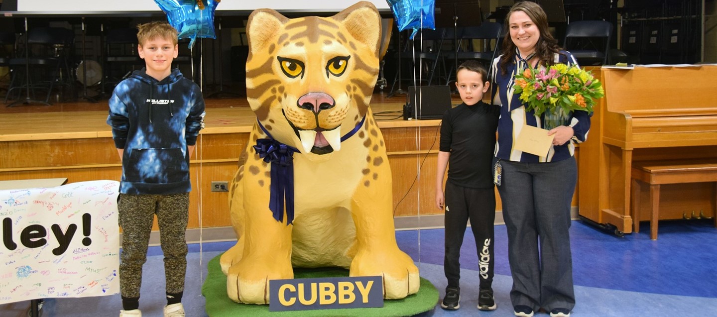 Two Brookside Elementary students stand on either side of the refurbished Cubby mascot with the teacher aide who fixed him up.