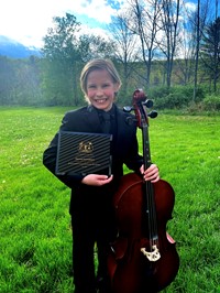 Young boy musician in a field with a plaque and his cello